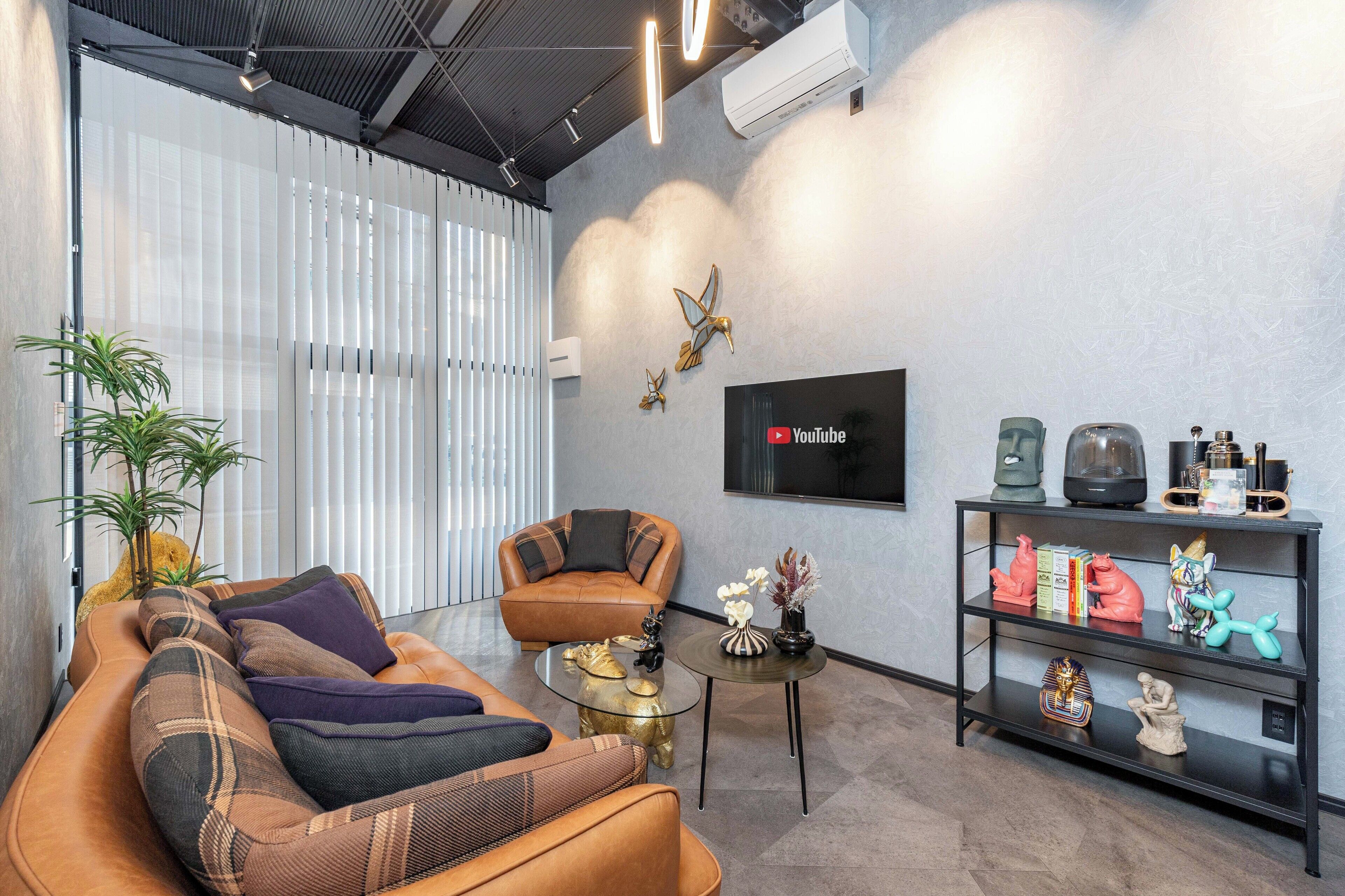 A modern living room with a leather sofa, a glass coffee table, and a black bookshelf with decorative items.