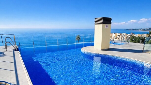 A clear blue infinity pool with a view of the ocean, a lifeguard tower, and a poolside area with a railing. - Luxury Duplex Infinity Pool - EHHouse (Estepona)