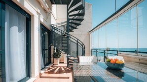 A balcony with a glass table, wicker chair, and a bowl of fruit. - Luxury Duplex Infinity Pool - EHHouse (Estepona)