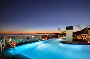 Una piscina amb una tanca de vidre, vista al mar i un capvespre.