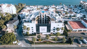 An aerial view of a coastal town with white buildings, a prominent modern building labeled "COSMO," and a clear view of the sea. - Luxury Duplex Infinity Pool - EHHouse (Estepona)