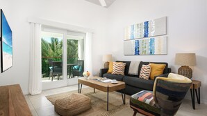 Ein modernes Wohnzimmer mit Sofa, Sesseln, Couchtisch und Blick durch eine Glastür auf einen Außenbereich.