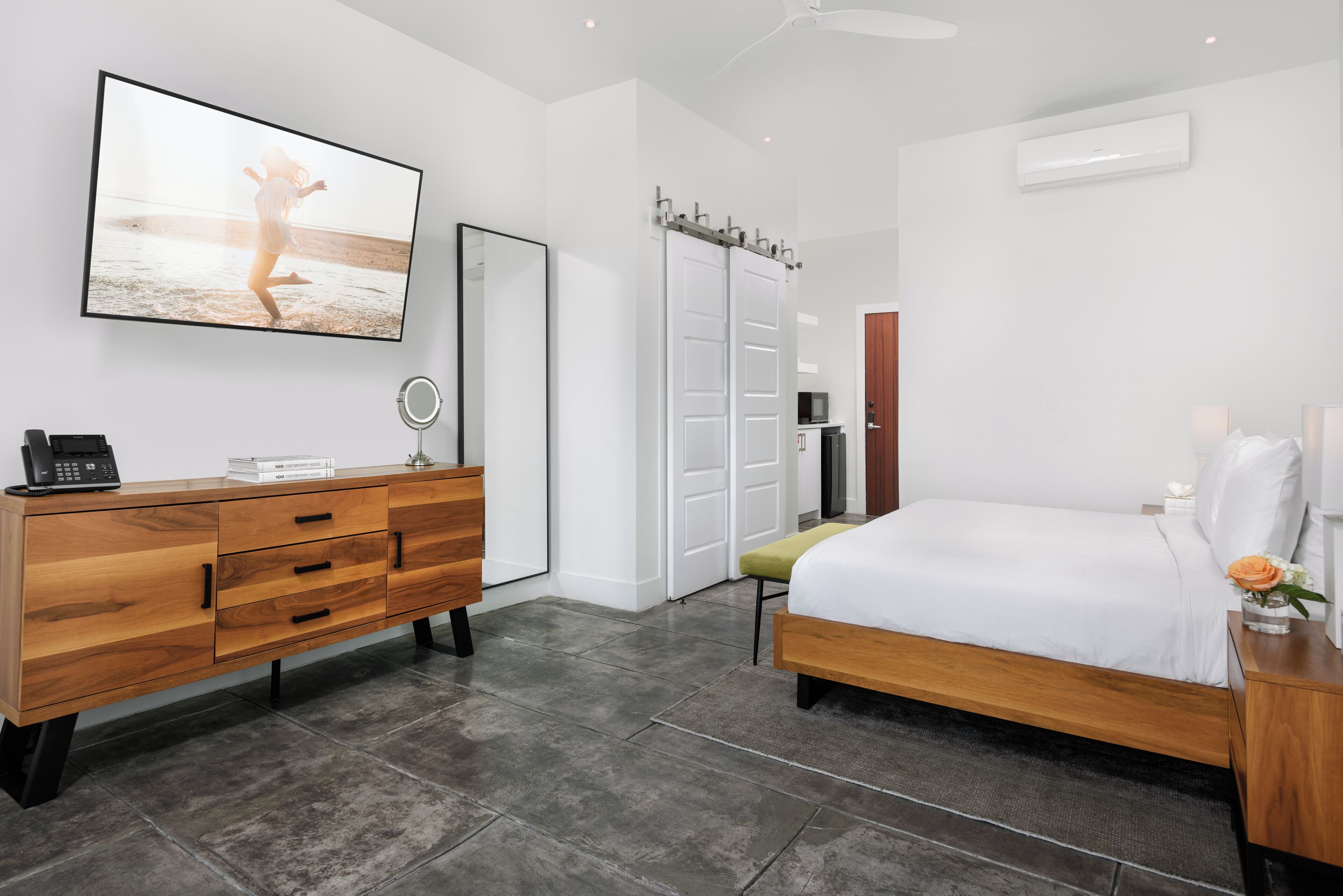 Un dormitorio con cama, cómoda de madera, televisor en la pared y puerta de baño.