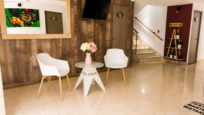 A hotel lobby with a wooden wall, a flat-screen TV, a staircase, and a sign indicating a garden. - Sol de Estadio (Medellín)