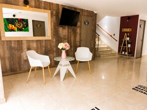 A hotel lobby with a wooden wall, a flat-screen TV, a staircase, and a sign indicating a garden. - Sol de Estadio (Medellín)