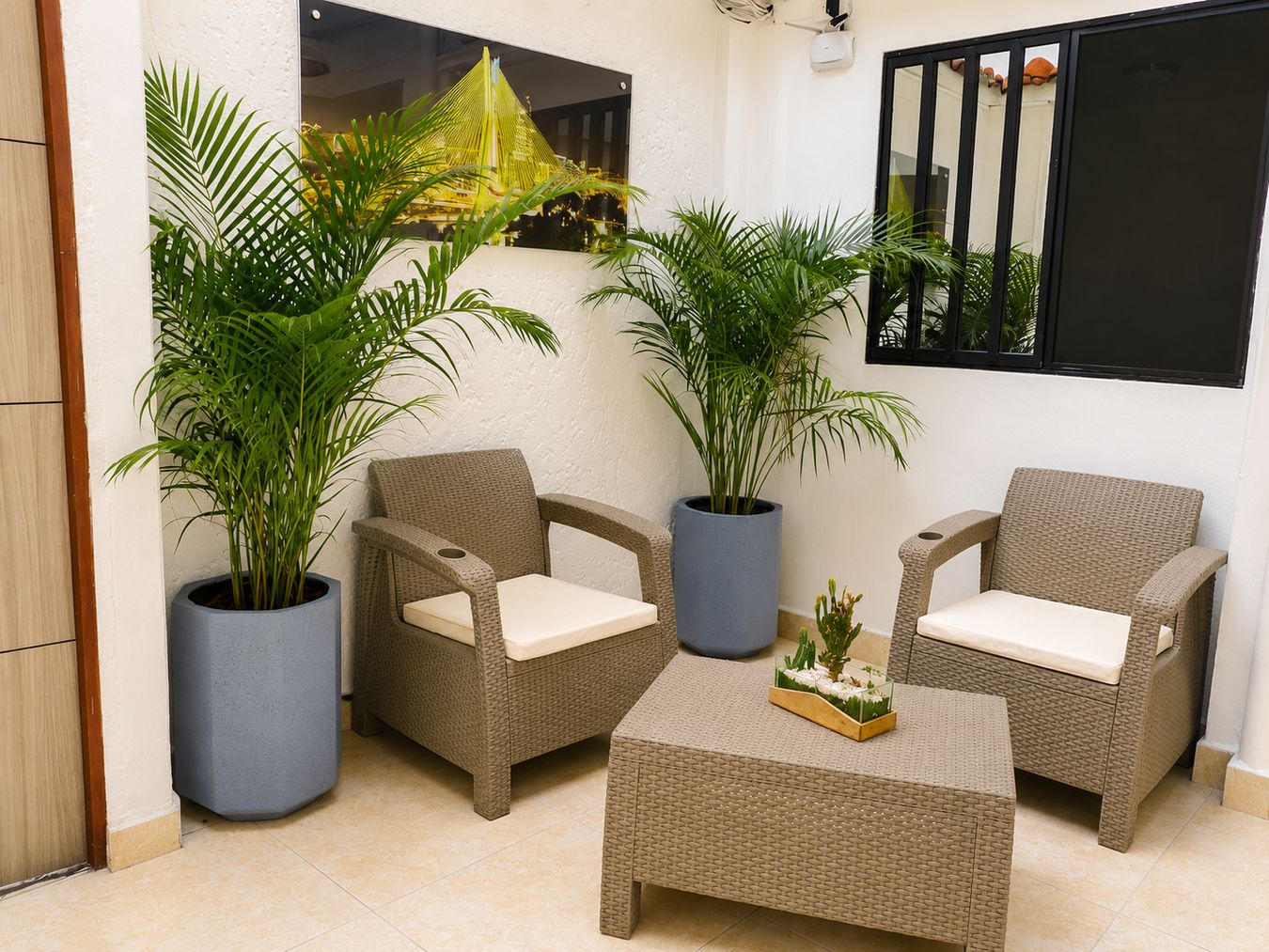 A room with two wicker chairs, a small table, and two large potted plants.