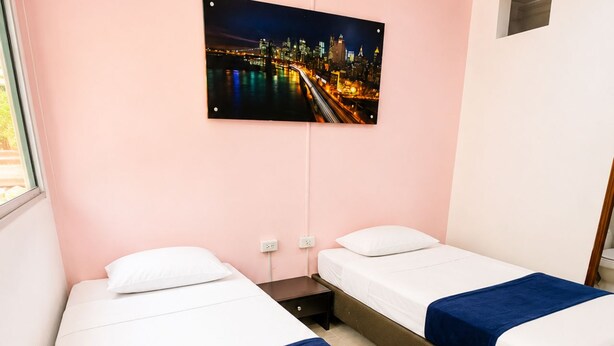 A hotel room with two beds, a night cityscape view, a small window, and a power outlet. - Sol de Estadio (Medellín)