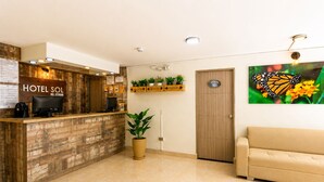 A hotel reception area with a wooden reception desk, a computer, a potted plant, a sofa, and a door marked '101'. - Sol de Estadio (Medellín)