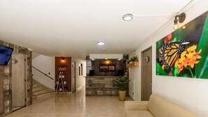 Um saguão de hotel com balcão de recepção, escada e um grande mural de borboletas na parede.