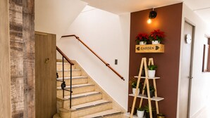 A staircase with a wooden handrail and beige steps, leading to a landing with a wall-mounted light fixture and a shelf with potted plants. - Sol de Estadio (Medellín)