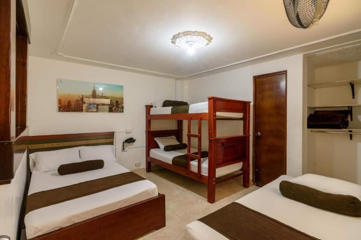 A hotel room with two single beds, a bunk bed, a wooden wardrobe, and a cityscape picture on the wall.