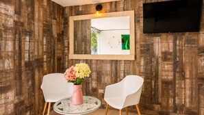 A room with wooden panel walls, a round glass table with a white chair, a pink vase with flowers, and a mounted mirror above the table. - Sol de Estadio (Medellín)