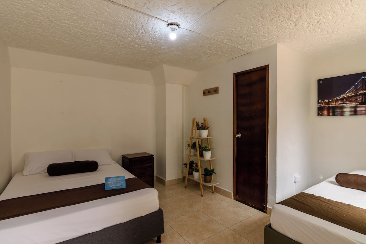 A hotel room with a bed, bedside table, lamp, and a wall-mounted painting.