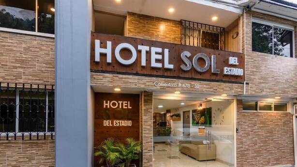 Um hotel moderno chamado "Hotel Sol Del Estadio", com uma placa de destaque, uma área de recepção e uma escadaria visível que leva à entrada.
