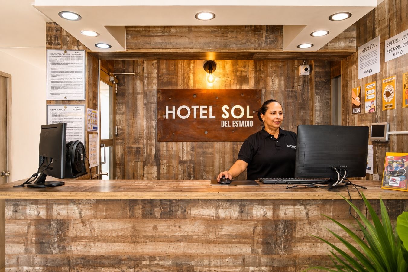 Mostrador de recepción en HOTEL SOL DEL ESTADIO con un fondo de madera, una computadora y un monitor.