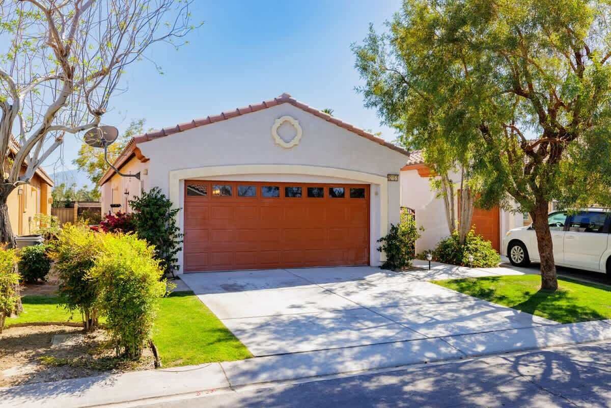 Une maison d’habitation avec une porte de garage rouge, un petit jardin devant et une voiture blanche garée dans l’allée.