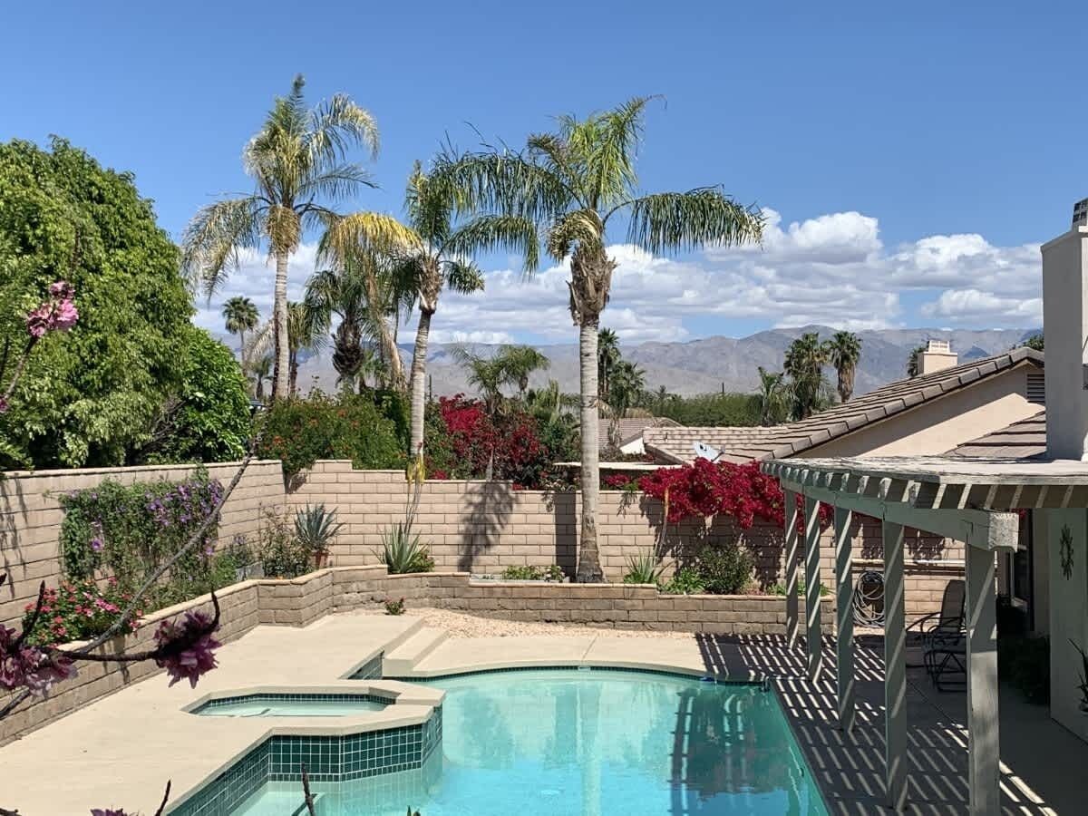 A pool area with a pergola, palm trees, and a view of mountains.