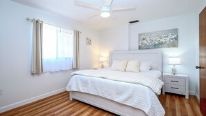 A bedroom with a bed, nightstands, a ceiling fan, and a window with curtains.