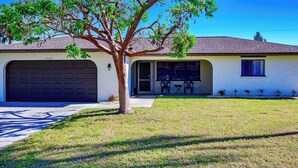 A single-story house with a garage, a tree in front, and a clear blue sky.
