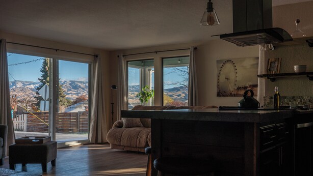 A spacious living area with a large sliding glass door leading to a balcony, a cozy seating area, and a kitchen with a view of the mountains.