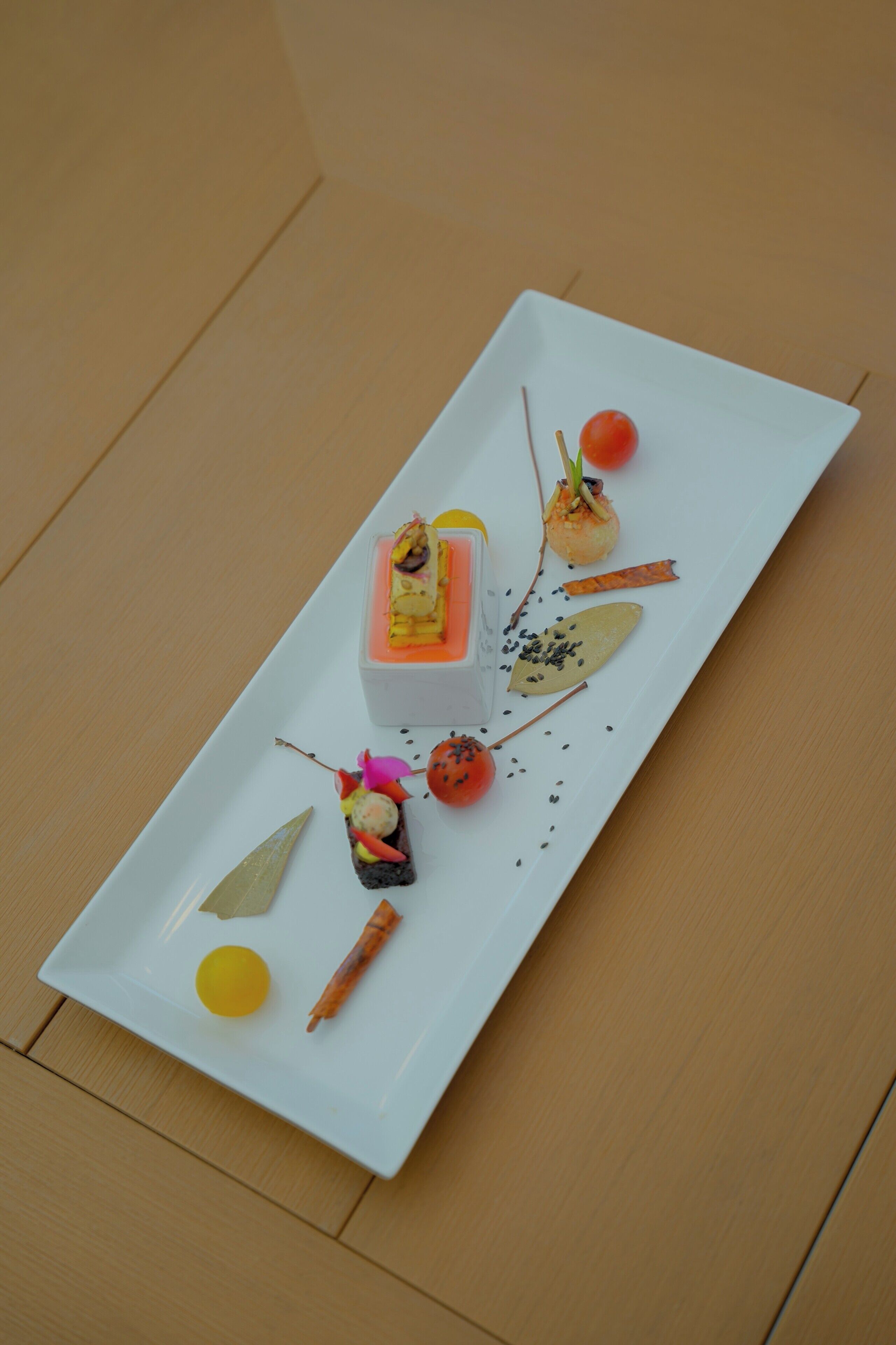 Ein weißer Teller mit verschiedenen Speisen, darunter eine kleine orangefarbene Frucht, eine gelbe Kugel und ein Nahrungsmittel mit einem grünen Blatt.