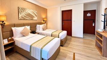 Quarto de hotel com duas camas, cabeceira de madeira, luminárias de cabeceira, ventilador de teto e piso de madeira.