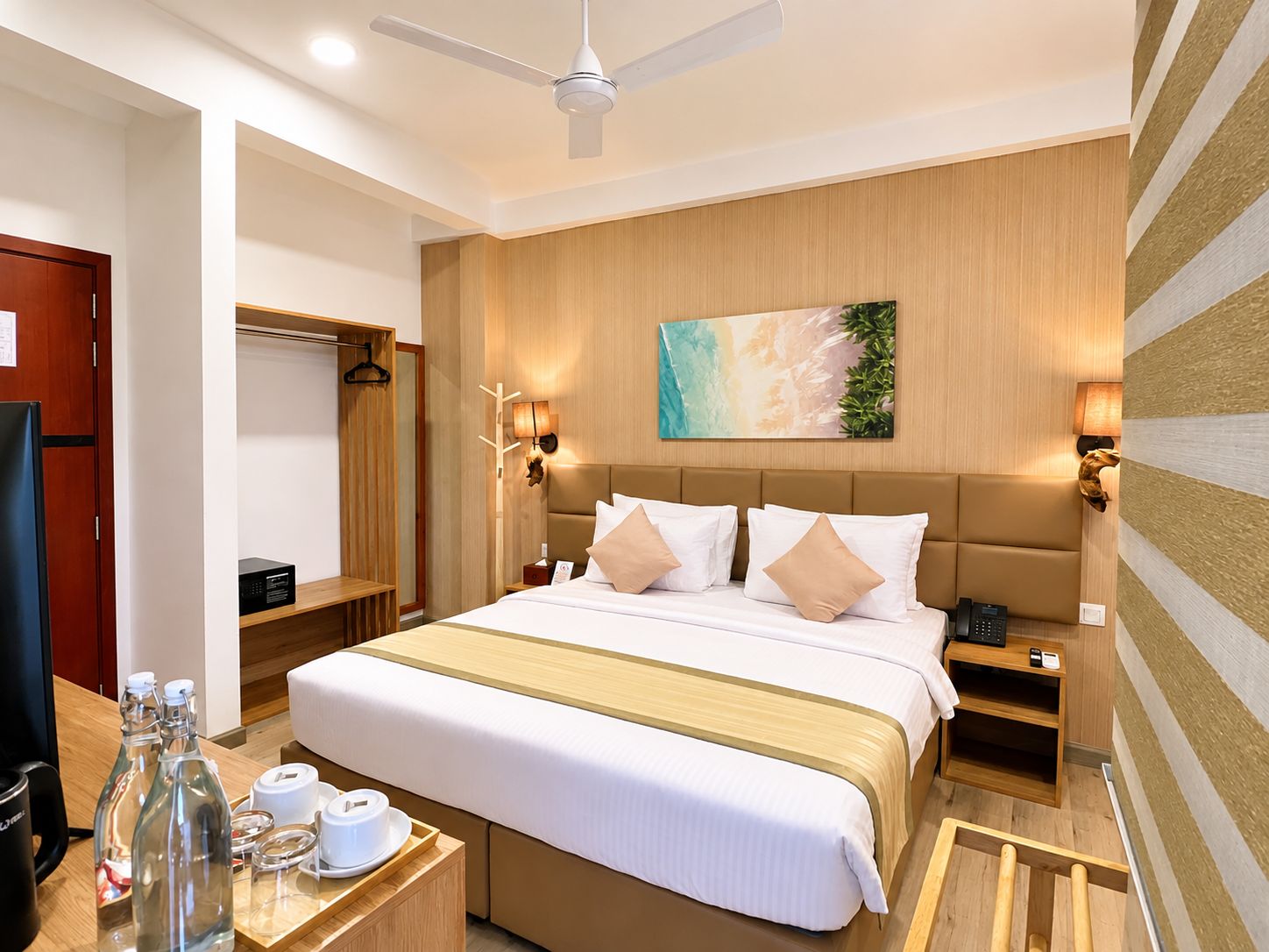 A hotel room with a bed, bedside tables, a wardrobe, a ceiling fan, and a painting on the wall.