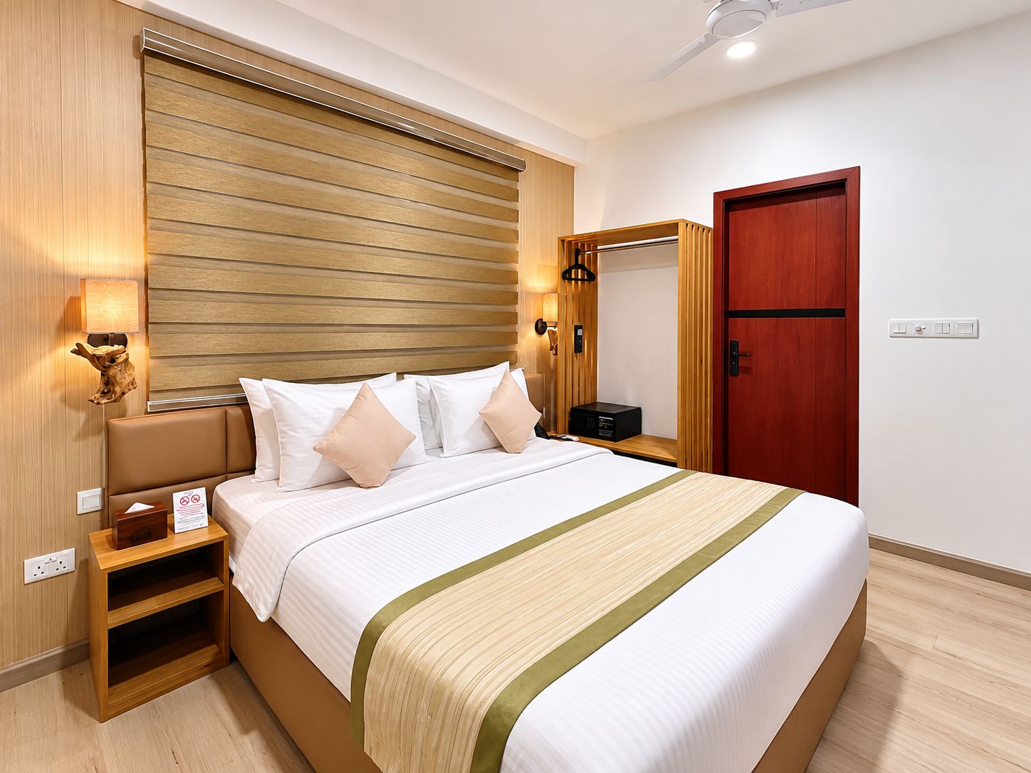 A hotel room with a bed, bedside tables, a mirror, a wooden headboard, and a door.