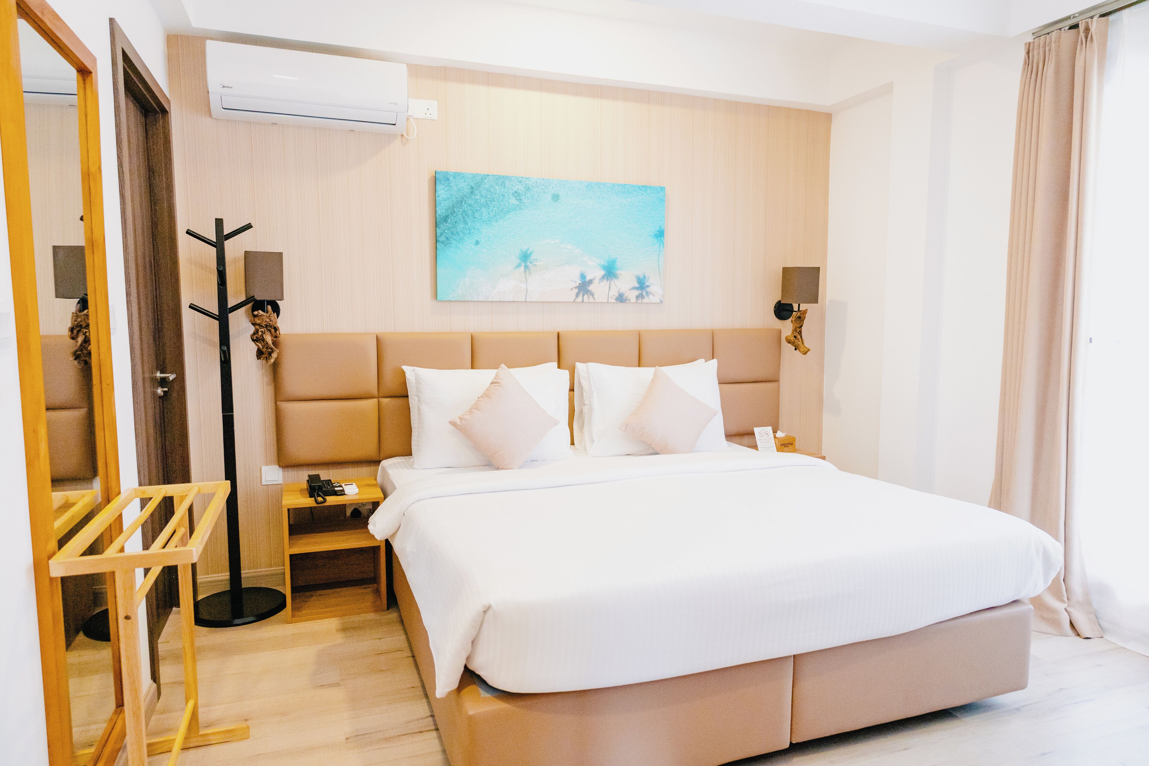 Una habitación de hotel con una cama grande, una mesita de noche, un perchero y un cuadro en la pared.