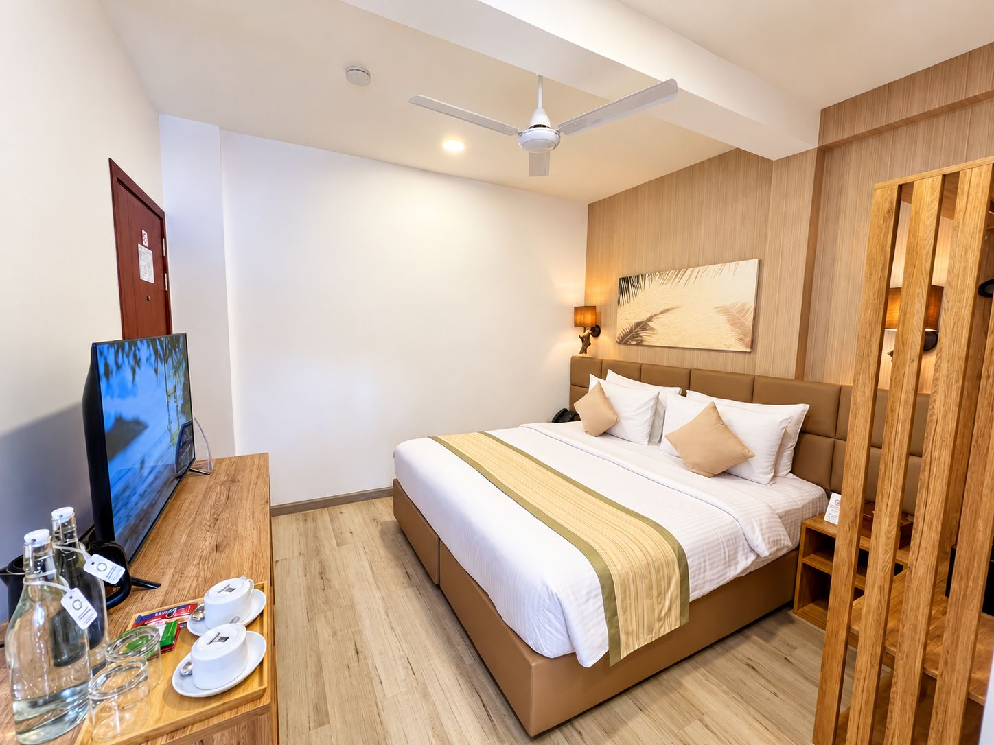 A hotel room with a bed, a TV, a desk with a computer, and a wooden wardrobe.