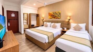 A hotel room with two beds, a desk, a TV, and a ceiling fan.