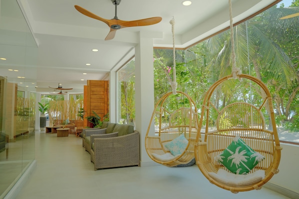 A spacious room with a large window, a hanging chair, and a sofa. - Cocomo Maldives (Himmafushi)
