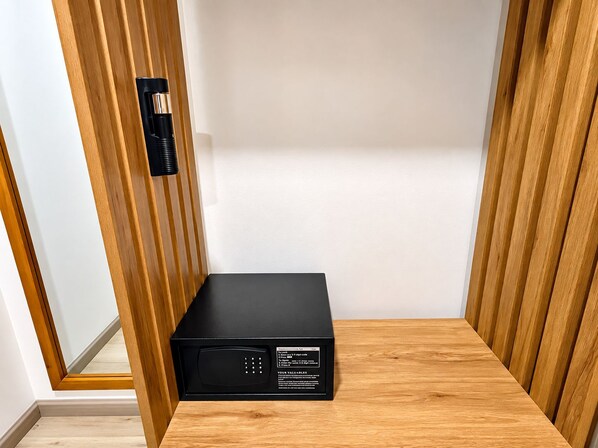 Un dispositivo electrónico negro sobre una repisa de madera en una esquina, con una pared blanca y un panel de madera.