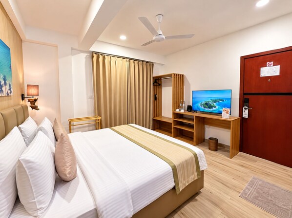 Une chambre d’hôtel comprenant un lit, un bureau avec une télévision, une armoire et un ventilateur de plafond.