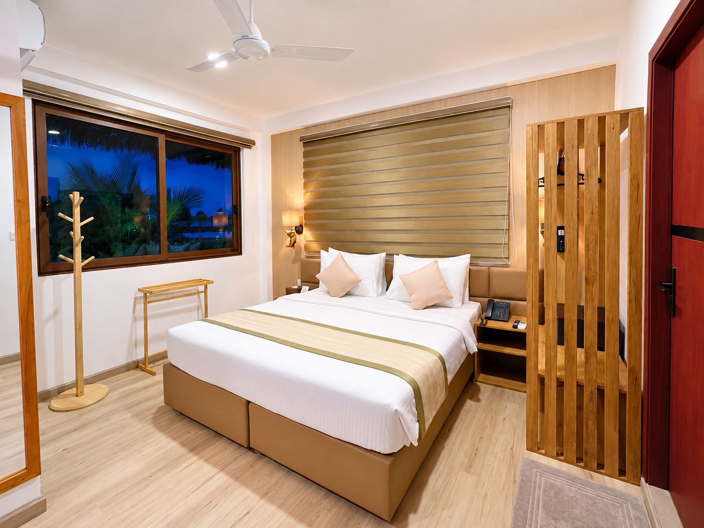 A modern hotel room with a large bed, a ceiling fan, a nightstand with a phone, and a view of the outdoors through a window.