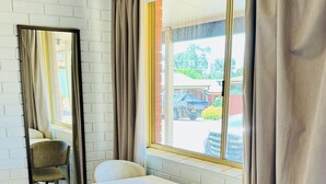 Een kamer met een witte baksteenmuur, een raam met gordijnen, een tafel en twee stoelen.