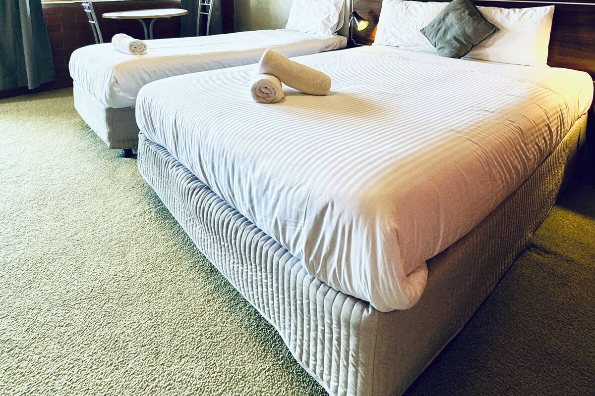 A hotel room with two beds, a small table, and a window with curtains.