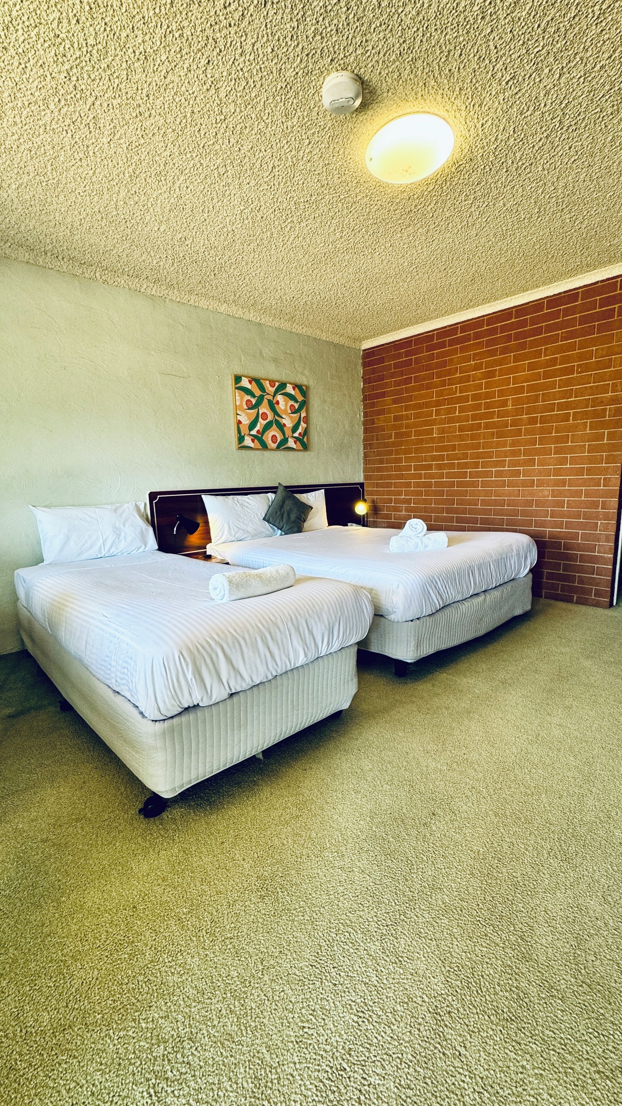 Une chambre d’hôtel avec deux lits, un mur en briques et un plafond à texture.