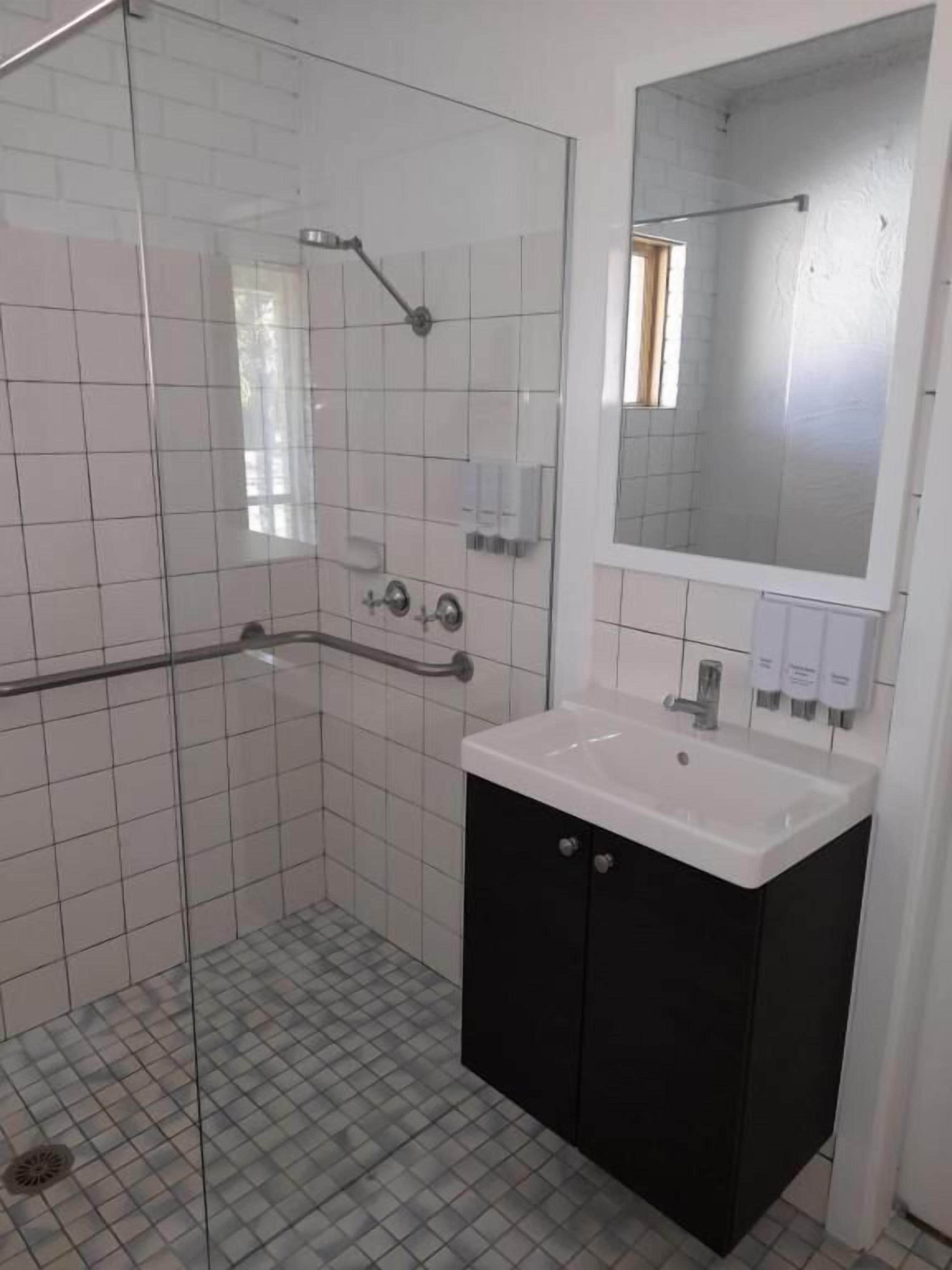 A bathroom with a glass shower enclosure, a white sink with a black cabinet, and a mirror above the sink.