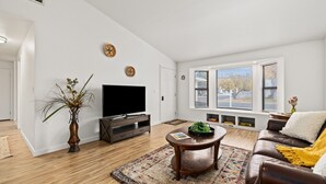 A modern living room with a flat-screen TV, a wooden coffee table, a brown leather sofa, and a large window with a view of trees. - Boise Foothills Boho Haven hosted by Boise BnB! (Boise)