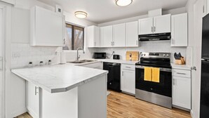 A modern kitchen with white cabinets, a central island, a black stove, and a microwave. - Boise Foothills Boho Haven hosted by Boise BnB! (Boise)