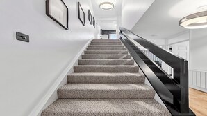 Un escalier dont les marches sont recouvertes de moquette et qui possède une rampe noire, menant à l’étage supérieur.