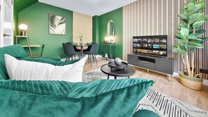 Un salon avec un canapé vert, une table à manger avec des chaises, un téléviseur et une plante en pot.