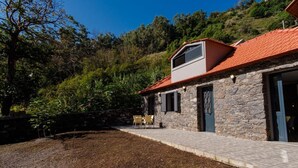 A stone building with a red-tiled roof, a small patio with chairs, and a garden area. - GuestReady - Tranquil Hideaway near Funchal (Funchal)