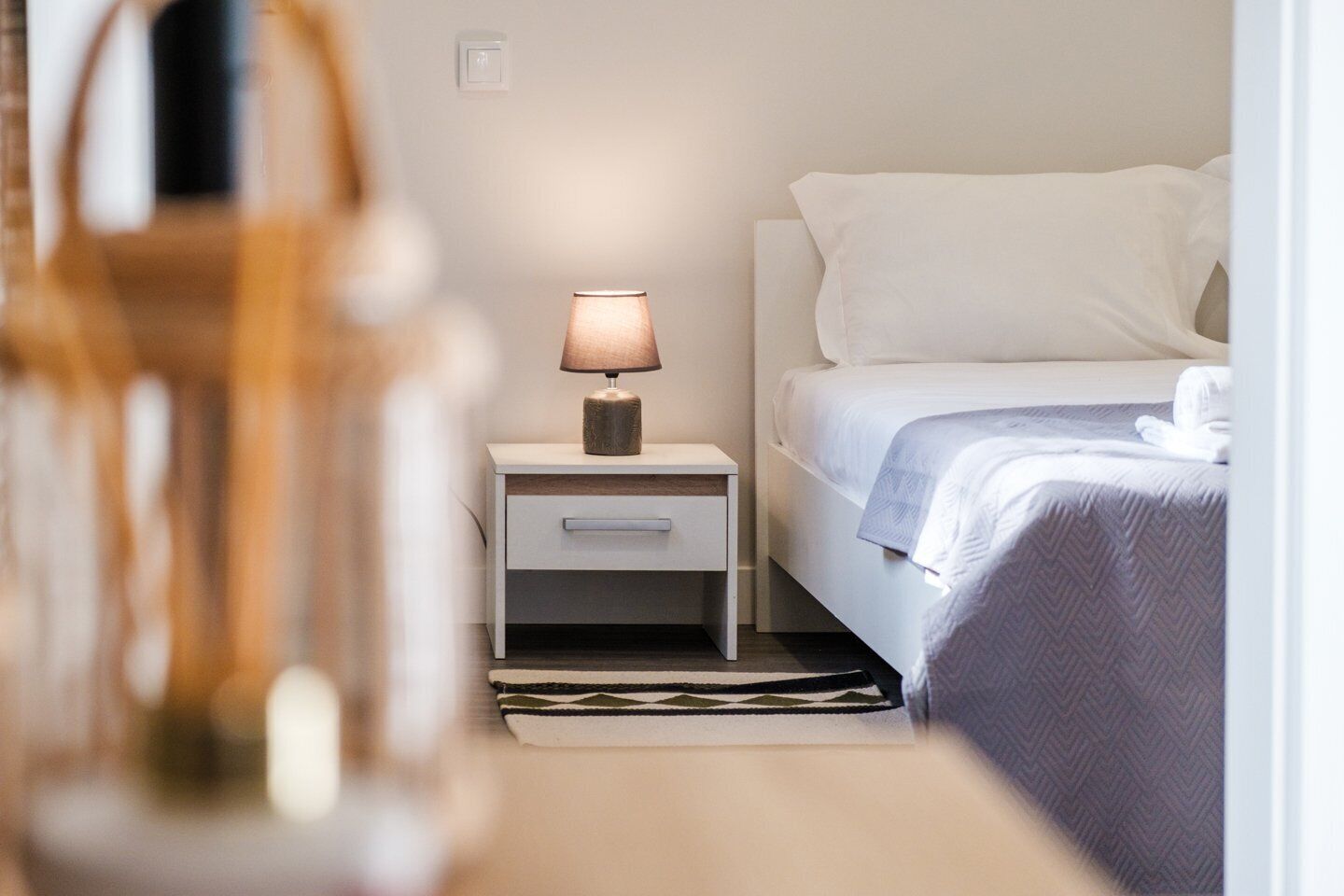 Une chambre d’hôtel bien rangée, avec un lit, une table de chevet dotée d’une lampe et un petit tiroir.