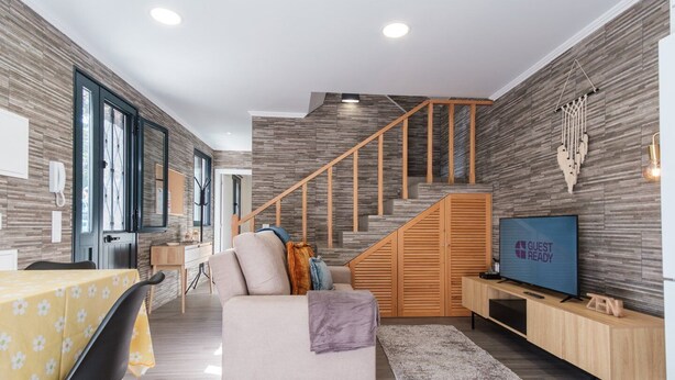 A modern living room with a sofa, TV, and wooden staircase. - GuestReady - Tranquil Hideaway near Funchal (Funchal)