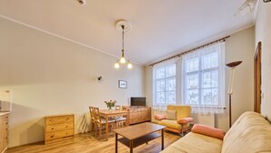 Un salon spacieux doté d’un plancher en bois, d’un canapé, d’une table à manger avec des chaises, d’un téléviseur et d’une fenêtre ornée de rideaux légers.