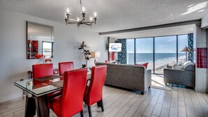 A modern living room with a large window, a dining area with red chairs, and a grey sofa. - Sweeping Ocean View from Each Bdr and Living Room, Safe and Quiet Neighborhood  (Myrtle Beach)