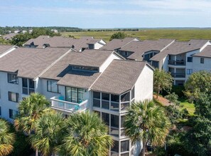 A multi-story residential building with balconies, surrounded by palm trees and a grassy landscape. - Osprey's Nest | Luxury Sea Palms Golf Condo St. Simons Island (Saint Simons Island)