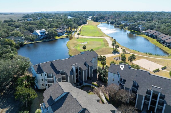 An aerial view of a residential area with a golf course, a lake, and multiple buildings.